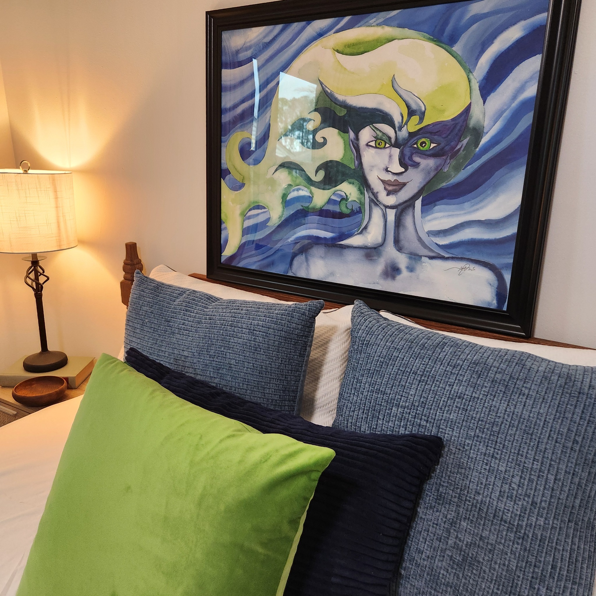 Framed blue and green figurative artwork displayed above a bed at Artful Ansley
